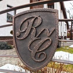 Kovaný erb s iniciálmi na modernej bráne pri rodinnom dome