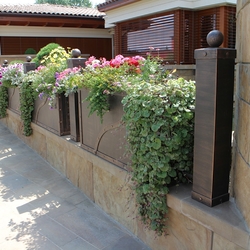 Kované kvetináče plné krásnych kvetov vsadené do plota - dizajnové oplotenie rodinného domu